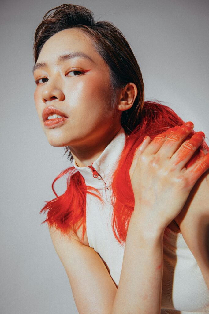Artistic portrait of a woman with red-toned hair and bold makeup, against a neutral background.